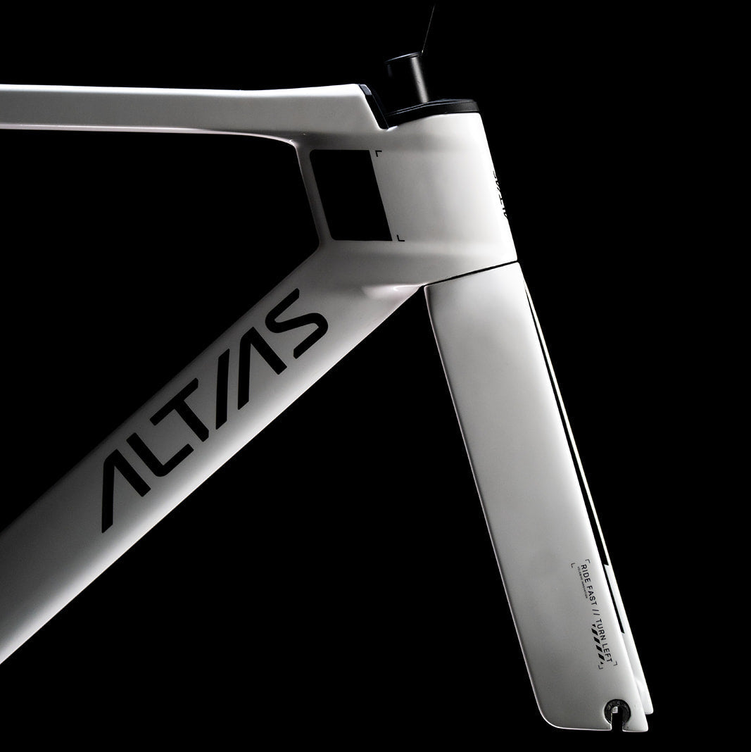 Close-up studio shot of a white bicycle frame section with the brand name ALTAS printed in black on the down tube, set against a solid black background.
