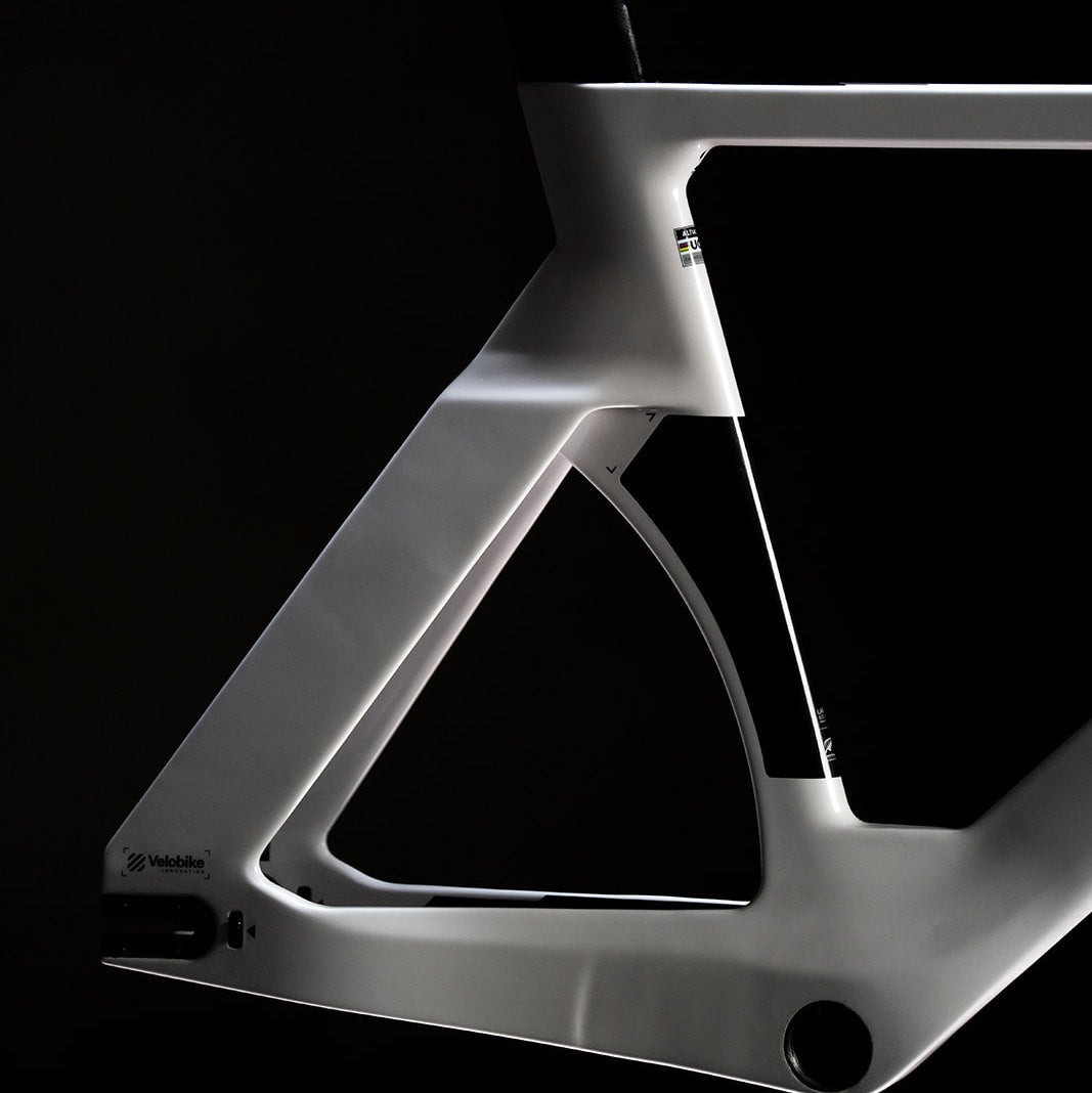 A close-up studio shot of a white carbon fiber bicycle frame against a solid black background, highlighting its sleek aerodynamic design and matte finish.